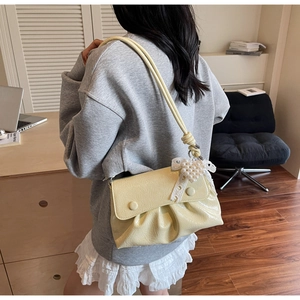Détail du sac plissé crème avec breloque cœur en perles et décoration de nœud en dentelle