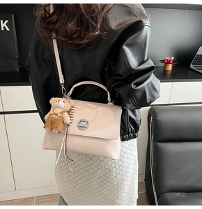 Close-up of beige crossbody bag with silver twist lock and cute teddy bear charm