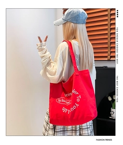 Detailed view of red canvas tote bag with white letter print styling on a casual outfit