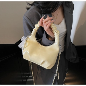 Detail of cream pleated handbag with lace bow, pearl charm and metal chain strap