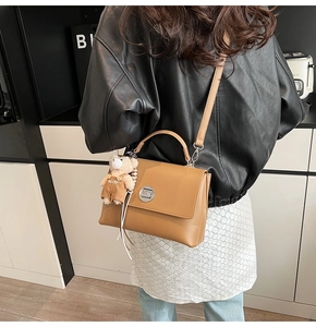 Detailed back view of a brown leather messenger bag with bear charm and metallic lock