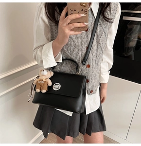 Detail of black crossbody bag with silver twist lock and cute teddy bear charm accessory