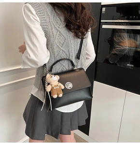 Detail of black leather crossbody bag with silver lock and plush bear pendant on model