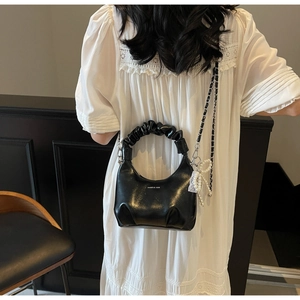 Detail of black pleated shoulder bag featuring pearl bow charm and logo branding