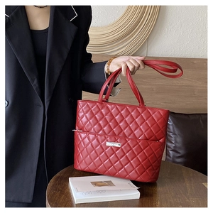 Detail of red quilted tote bag with silver logo plate and spacious diamond pattern design