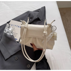 Détail d'un sac à main blanc crème plissé avec poignées à nœuds et breloque en perles