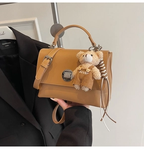 Detail of tan square crossbody bag with a cute bear charm and silver twist lock closure