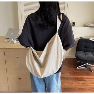 Close-up of a large beige woven tote bag styled as a relaxed crossbody shoulder bag