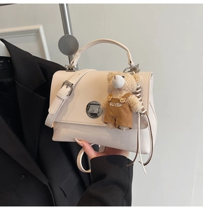 Detail of cream faux leather shoulder bag with silver turn-lock and cute bear charm