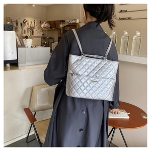 Rear view of silver metallic quilted backpack worn by a model in a modern cafe setting
