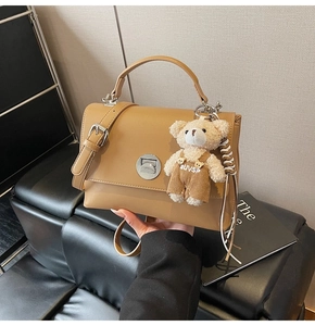 Close-up of camel leather handbag with silver twist lock and cute plush bear charm accessory