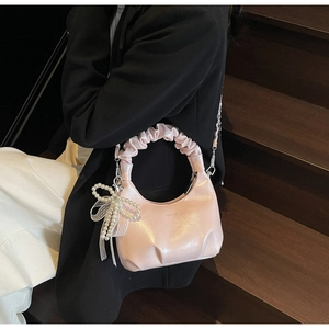 Detail of pearl pink pleated handbag with decorative pearl bow and chic metal chain strap