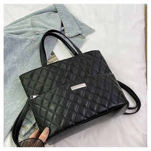 Detail of black quilted tote bag showing shiny texture and silver metallic logo plate