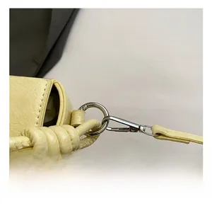 Détail du crochet métallique et de la bandoulière en cuir jaune clair du sac carré