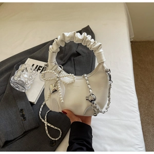 Detail of white ruched handbag featuring pearl bow, heart charm and leather-interwoven chain