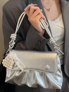 Sac à main plissé argenté avec breloque cœur en perles, porté par un mannequin en gris