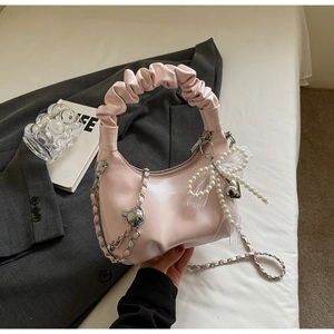 Detail of light pink moon bag featuring pleated handle and pearl bow charm accessory