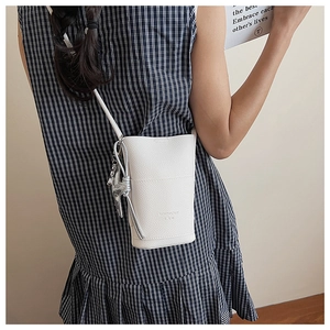 Close-up of a white pebble leather mini crossbody bag with a slim strap on a model