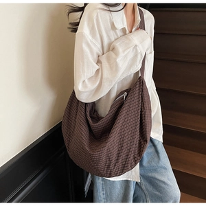 Detailed side view of large brown woven crossbody bag worn by a model on stairs