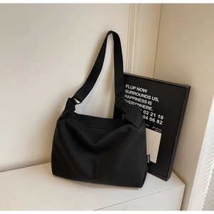 Close-up of minimalist black canvas shoulder bag with wide adjustable strap on white table