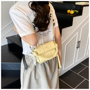 Détail du sac tressé jaune clair avec larges lanières en cuir et pendentif en dentelle