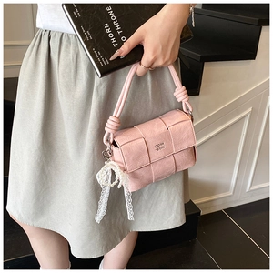 Détail du sac tressé rose avec poignée nouée, nœud en dentelle et breloque perle