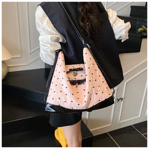 Detail view of pink bow tote bag with black straps and heart charm in a modern setting