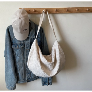 Detailed close-up of ivory woven tote bag with 3D bubble texture hanging on wood hook