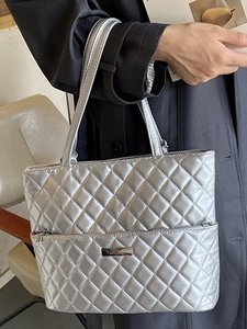 Silver quilted tote bag with diamond pattern and metal logo plate shown in use
