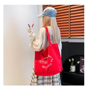 Detail of red canvas tote bag with white art lettering and large storage capacity