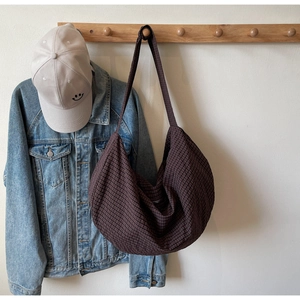 Detail of large woven hobo bag in dark brown plaid fabric hanging on a wooden hook