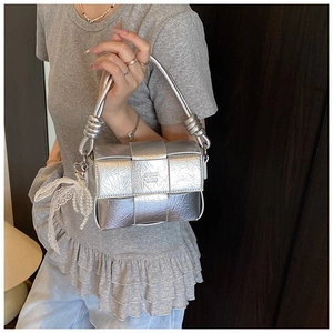 Détail du sac à main tressé argenté avec poignée nouée et breloque en dentelle de perles