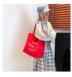 Detail view of large red canvas tote bag with white lettering on female model shoulder