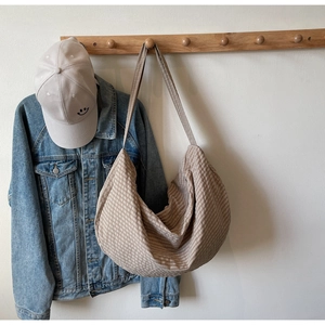 Detail of a beige checkered woven tote bag hanging on a wooden hook in a minimalist setting