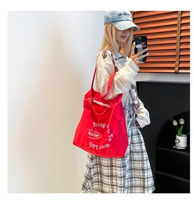 Detailed close-up of a red canvas tote bag with white Atelier lettering and wide shoulder strap