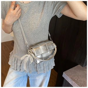Détail d'un sac tressé argenté avec nœud en dentelle et pendentif en perles