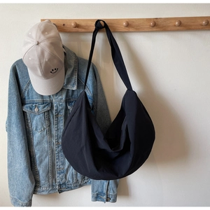 Detail shot of black crescent woven tote bag hanging on wooden hook with casual props