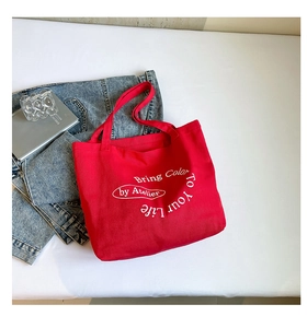 Detail shot of a red canvas tote bag with white lettering on a stylish desktop setup