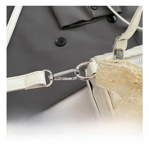 Close-up of white quilted cylinder bag with silver hook and lace bow decoration