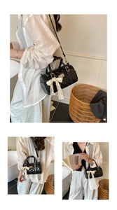 Detail of black quilted barrel bag featuring cream lace bow and sleek faux leather finish