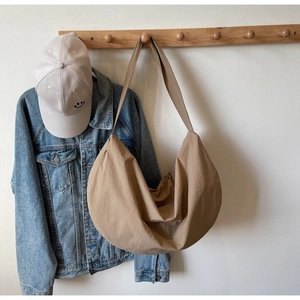 Detail of an earth-toned oversized woven crescent bag hanging on a wooden hook