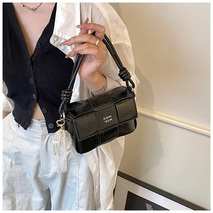Détail d'un sac à main noir tressé avec breloque perle et accessoire en dentelle