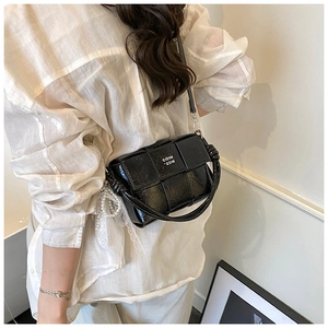 Détail d'un sac à main noir verni avec pendentif perle et poignée tissée