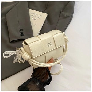 Détail du sac à main tressé crème avec poignée nouée et breloque élégante en dentelle
