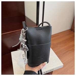 Detail of minimalist black pebbled leather phone bag with silver dog charm and tassels