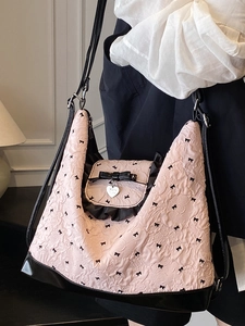 Pink tote bag with black bow print and heart pendant shown on a model's shoulder