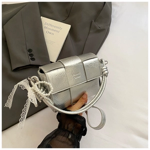 Détail d'un sac à main tressé argenté avec bandoulière perle et ruban en dentelle