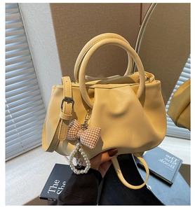 Detail of light yellow pleated handbag with pearl bow charm and round handles