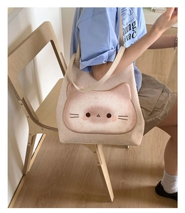 Detailansicht der beigen Canvas-Tasche mit Katzenmotiv, getragen von einem Model auf Holzstuhl