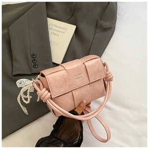 Détail du sac bandoulière rose en cuir PU tissé avec logo argenté et breloque en dentelle